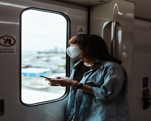 Person holding a smartphone while commuting, looking out the window of public transport
