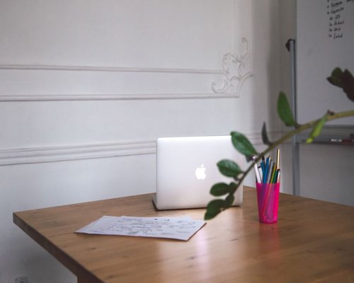 A clean desk set up for an online meeting, with a notebook, pen, and natural light